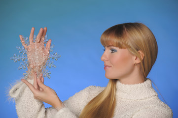 long-haired blonde in the studio on a blue background with a snowflake in her hands, winter concept