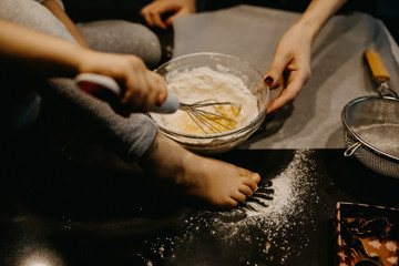 Little girl mixing flour with eggs, making dough. Mother and little daughter baking cookies at home.