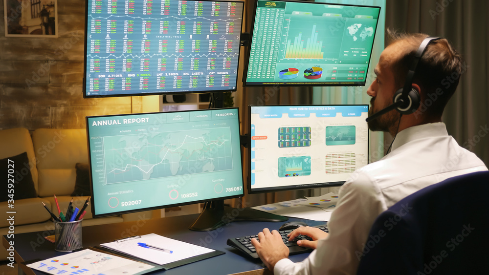 Poster back view of stock market trader looking at graphs on multiple monitors from home office.