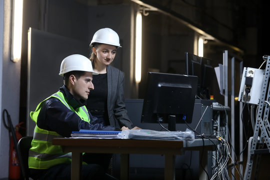 Portrait of a female factory manager in a white hard hat and business suit and factory engineer in work clothes. Controlling the work process in a factory.
