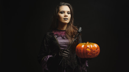 Fototapeta na wymiar Young woman dressed up like a witch for halloween holding a scary pumpkin over black background