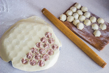 Traditional russian uncooked pelmeni on cutting board and ingredients for homemade pelmeni on white table. Process of making pelmeni, ravioli or dumplings with meat. Copy space. Side view.