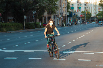 Chica joven de ojos claros, yendo en bicicleta durante coronavirus en una ciudad.