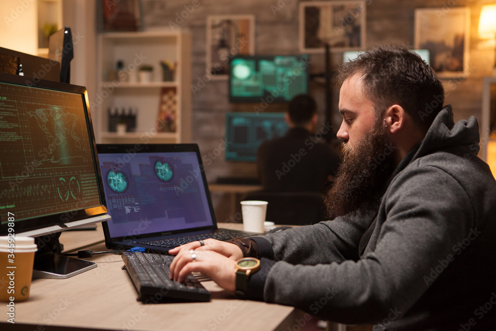 Poster adult hacker typing a virus on computer to break firewall security. young hacker in the background.