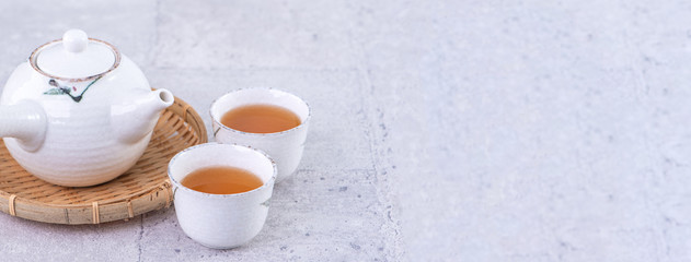 Hot tea in white teapot and cups on a sieve over bright gray cement background, closeup, copy space...