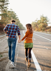 Young couple of man and woman running outdoors, holding hands, on an asphalted empty road.