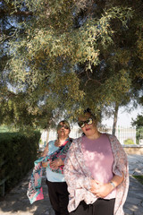 Two women, covered with colorful scarves under green trees in Cyprus