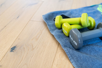 Fitness at home, equipment and tools for gym at home. Green dumbbell with towel, mobile phone on wooden parquet floor. Background with copyspace for sport activity at home with accessories.