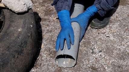 A plumber in rubber gloves cut a plastic sewer pipe lengthwise into two halves.