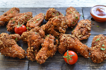 Baked chicken wings with sesame seeds. Ketchup and chili sauce. Free space for text. Wooden background. Delicious fried chicken wings. Close up