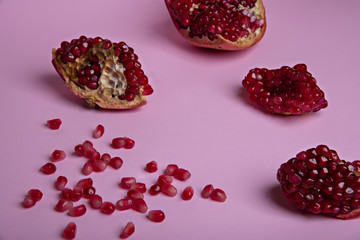 Broken red ripe pomegranate fruit on the pastel pink background. Selective focus.