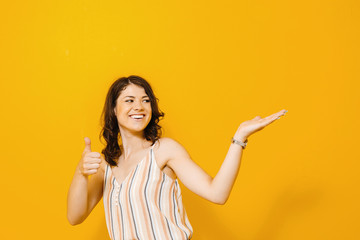 Image of excited young asian woman standing isolated over yellow background make winner gesture.