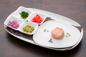 A tuna pate with tomatoes, cucumbers, onions and parsley in white ceramic plates on a wooden table