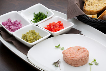 A tuna pate with tomatoes, cucumbers, onions and parsley in white ceramic plates with homemade bread in the background