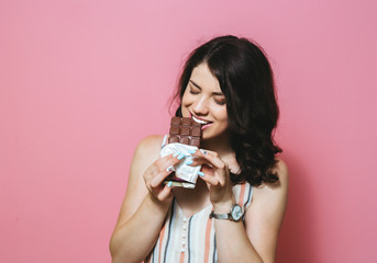 Image of happy cute Asian young woman standing isolated over pink background eating chocolate.