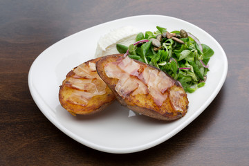 Baked potatoes with bacon, fresh cheese and a salad in a ceramic plate on a wooden table