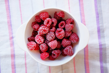 Frozen raspberries in a white bowl on a traditional textile towel. Vegetarian and healthy concept.