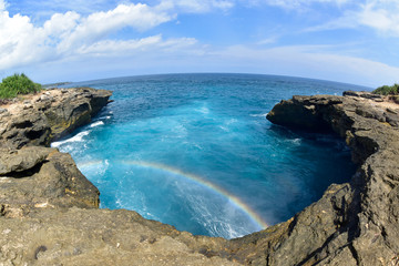 There's a rainbow over the sea looking down from the cliffs. Devils tears on rembongan island
