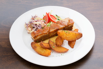 Pork ribs with roasted potatoes, cabbage and lettuce in a white ceramic plate on a wooden table