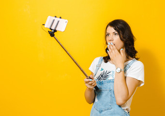 Portrait of a happy young girl making selfie isolated over yellow background