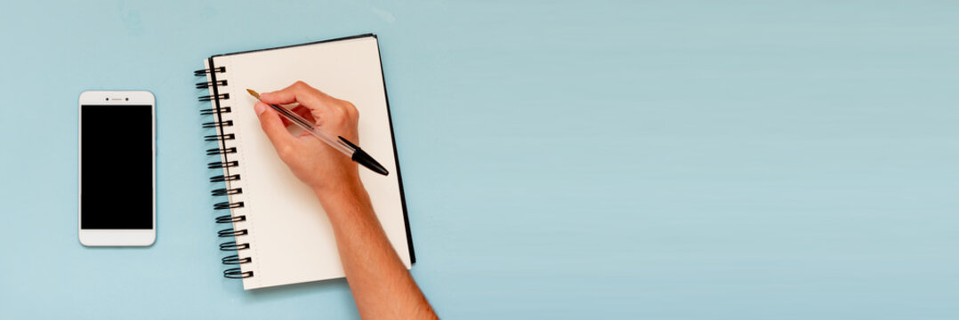 Businesswoman hand writing on notebook with phone. Layout with copy space, desktop of a student