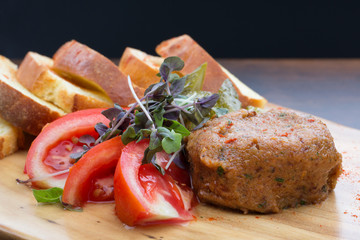 Steak tartare with tomatoes, cucumbers and sliced homemade bread on a wooden board