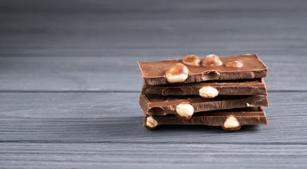 Stack of milk chocolate pieces with nuts on gray wooden table. Pile of chocolate bars Chocolate pieces with big hazelnut