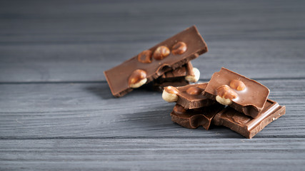 Pieces of milk chocolate with nuts on a gray wooden table. Chocolate bars with hazelnut. Sweet brown chocolate stack.