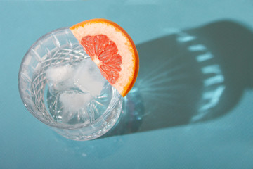 Gin tonic with ice and grapefruit top view. Glass with strong shadows on blue background. 