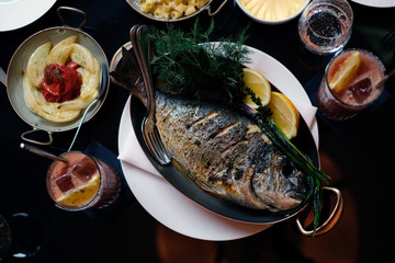 Flame grilled whole seabream served as a Sunday roast in a fish restaurant with side dishes and cocktails