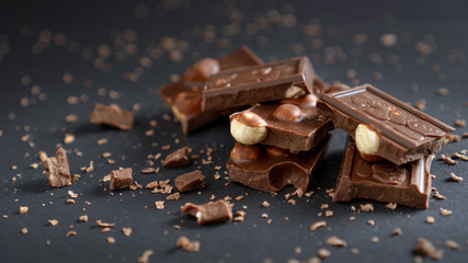 Milk chocolate with hazelnut and crumbs on a black background Closeup stacked slices of chocolate, nuts and crumbs bokeh
