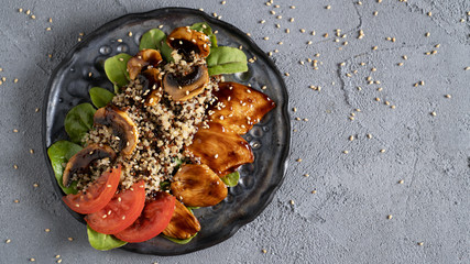 Healthy quinoa salad with spinach tomato chicken breast and mushrooms in teriyaki sauce and sesame seeds on black plate