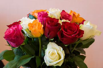 Lovely big colorful bouquet with many flowers  roses of red, vinous, orange and white colors. Green leaves and thorns. Still life. Calm pink background