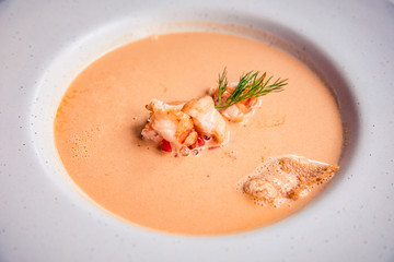 Closeup of creamy lobster bisque soup with grilled prawn and dill in white bowl