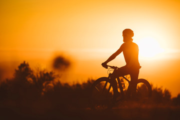 Fototapeta na wymiar Silhouette of a cyclist man riding mountain bike on a mountain at sunset.