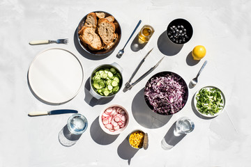 Photo of a fresh spring salad on a white porcelain plate and vegetable mix of ingredients in metal bowl on a white rustic background sunlight with shadows
