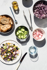 Photo of a fresh spring salad on a white porcelain plate and vegetable mix of ingredients in metal bowl on a white rustic background sunlight with shadows
