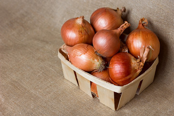 Golden onion round in a wicker basket, a wooden box on a background of natural homespun half a dozen napkins, useful vegetable vitamins, copy space for text