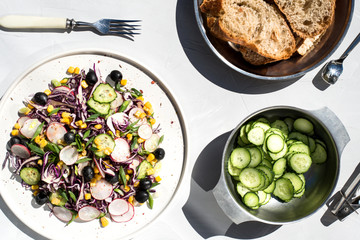 Photo of a fresh spring salad on a white porcelain plate and vegetable mix of ingredients in metal bowl on a white rustic background sunlight with shadows
