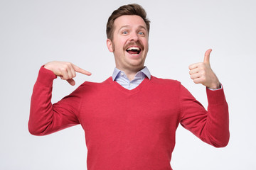 man shows himself with thumbs, smiles satisfied happy, pointing oh his chest bragging.