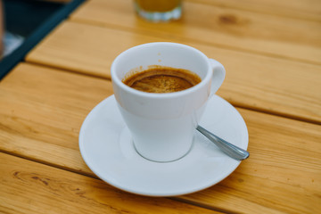 Americano in a white cup on a wooden table. Delicious morning coffee in a summer cafe. White cup with coffee on a plate.