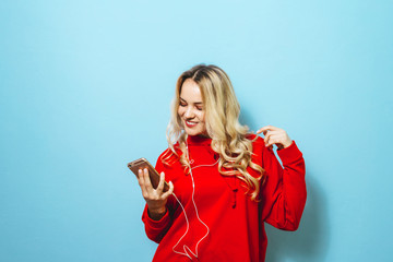 Image of a beautiful blonde excited  girl listening to music in headphones and dancing over blue background