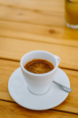 Obraz premium Americano in a white cup on a wooden table. Delicious morning coffee in a summer cafe. White cup with coffee on a plate.