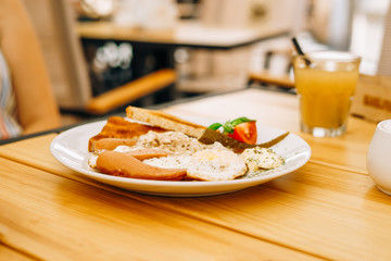 Delicious breakfast in the cafe: scrambled eggs and a glass of juice. Scrambled eggs with sausages, tomatoes and cheese. Scrambled eggs with ham and toast on a white round plate