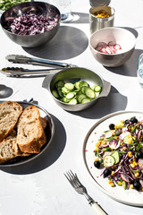 Photo of a fresh spring salad on a white porcelain plate and vegetable mix of ingredients in metal bowl on a white rustic background sunlight with shadows
