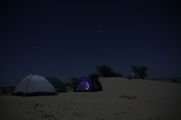 kilka namiotów biwakujących na dzikiej plaży późnym wieczorem pod granatowym gwieździstym...