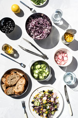 Photo of a fresh spring salad on a white porcelain plate and vegetable mix of ingredients in metal bowl on a white rustic background sunlight with shadows
