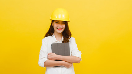 Young Asian woman engineer using digital tablet with positive expression, dressed in casual clothing and looking at camera over yellow background. Happy adorable glad woman rejoices success.