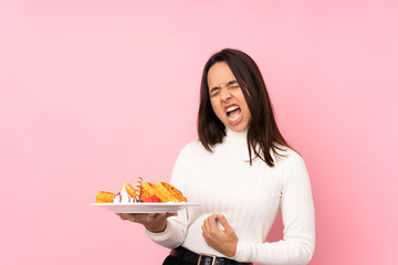 Young brunette woman holding waffles over isolated pink background making guitar gesture