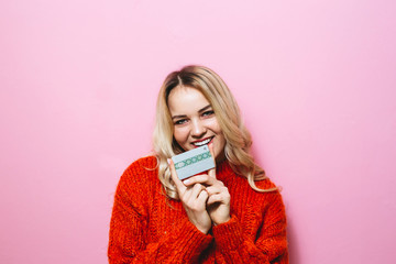 Portrait of a blond girl holding a credit card and smiling in the room on a pink background